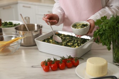 Photo of Woman making spinach lasagna at marble table indoors, closeup