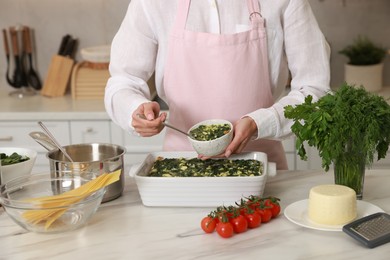 Photo of Woman making spinach lasagna at marble table in kitchen, closeup