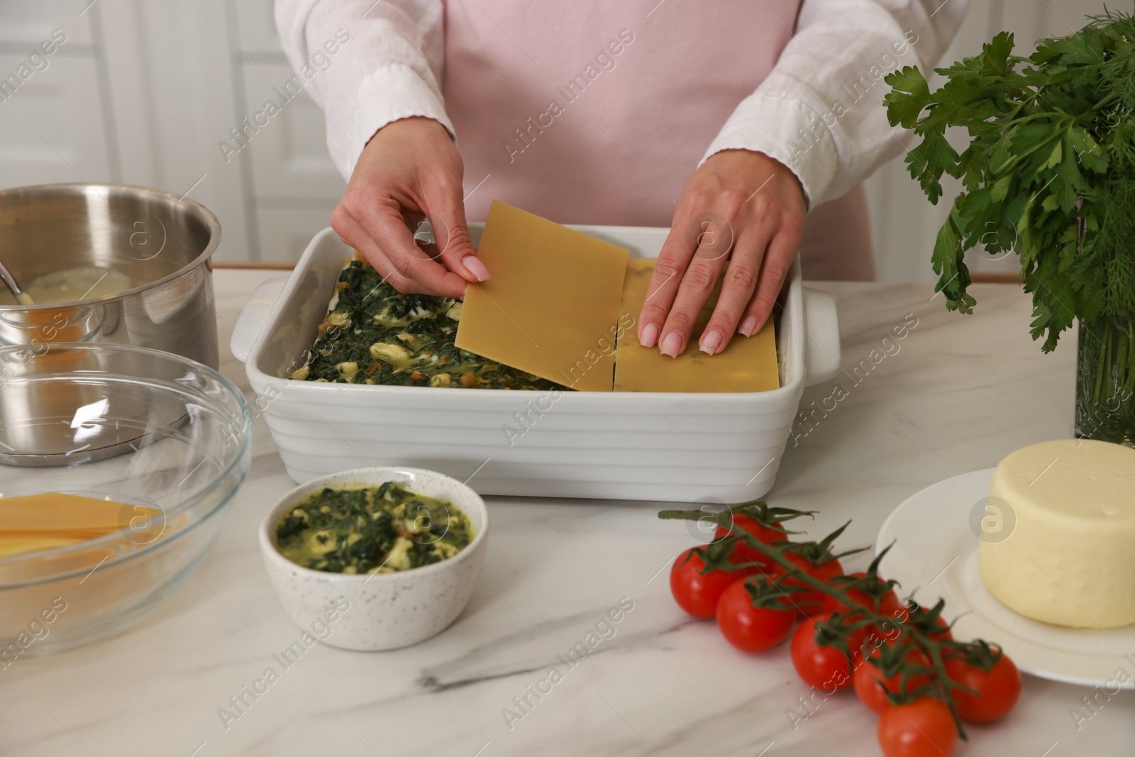 Photo of Woman making spinach lasagna at marble table indoors, closeup