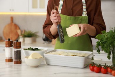 Photo of Woman grating cheese onto spinach lasagna at marble table indoors, closeup