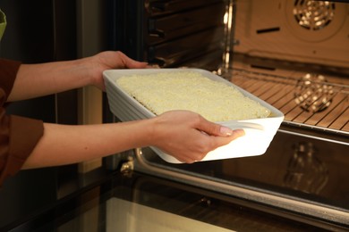 Photo of Woman putting baking dish with spinach lasagna into oven, closeup