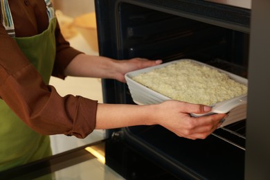 Photo of Woman putting baking dish with spinach lasagna into oven indoors, closeup