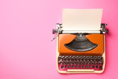 Photo of Vintage typewriter with sheet of paper on pink background, top view. Space for text
