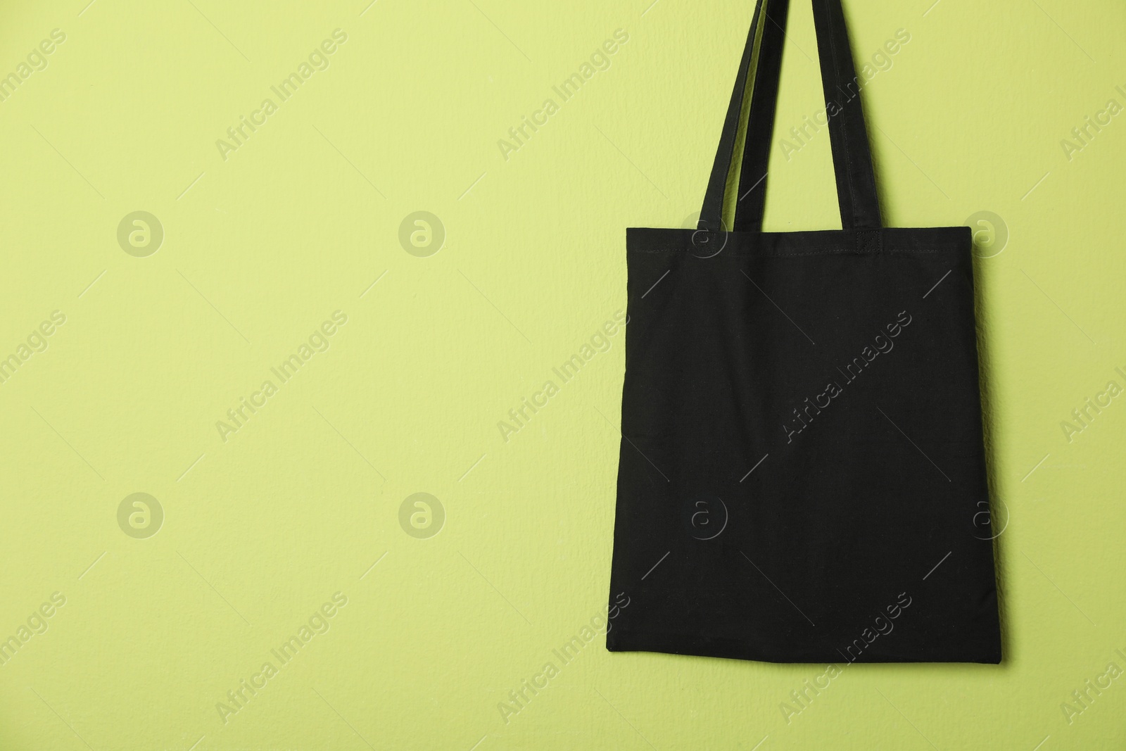 Photo of Black eco bag hanging on green wall. Mockup for design