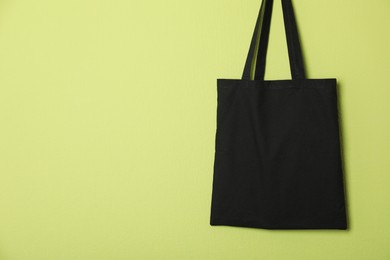 Photo of Black eco bag hanging on green wall. Mockup for design