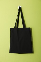 Photo of Black eco bag hanging on green wall. Mockup for design