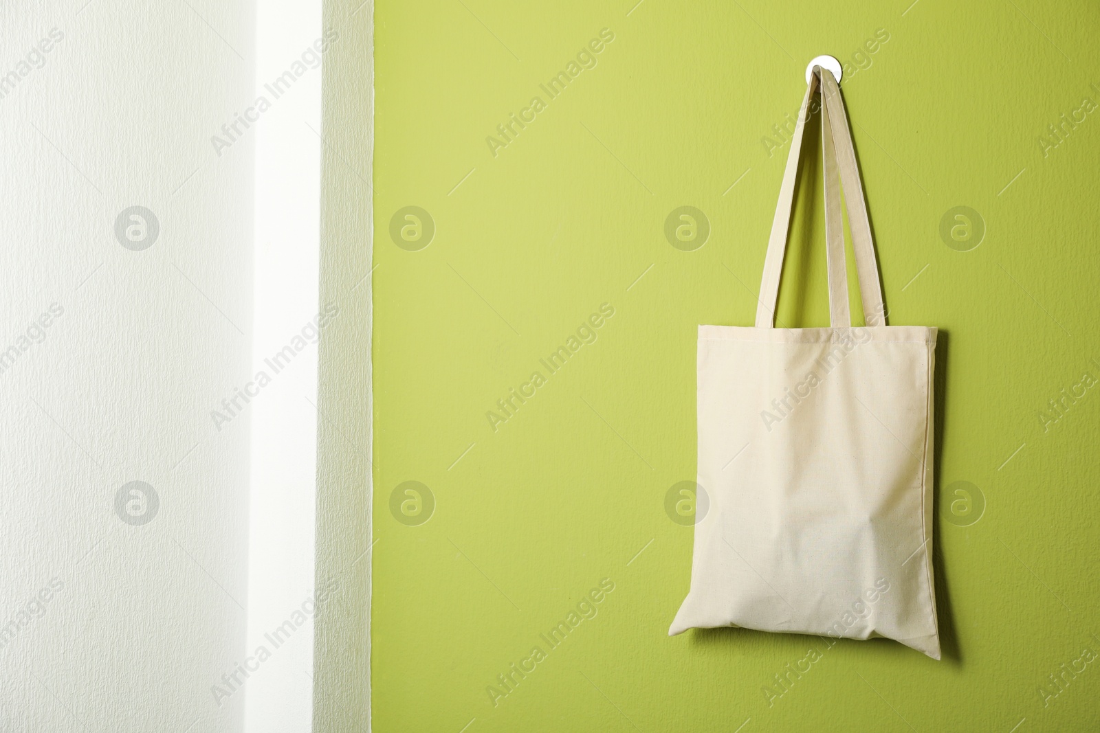 Photo of One eco bag hanging on green wall. Mockup for design