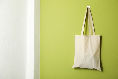 Photo of One eco bag hanging on green wall. Mockup for design