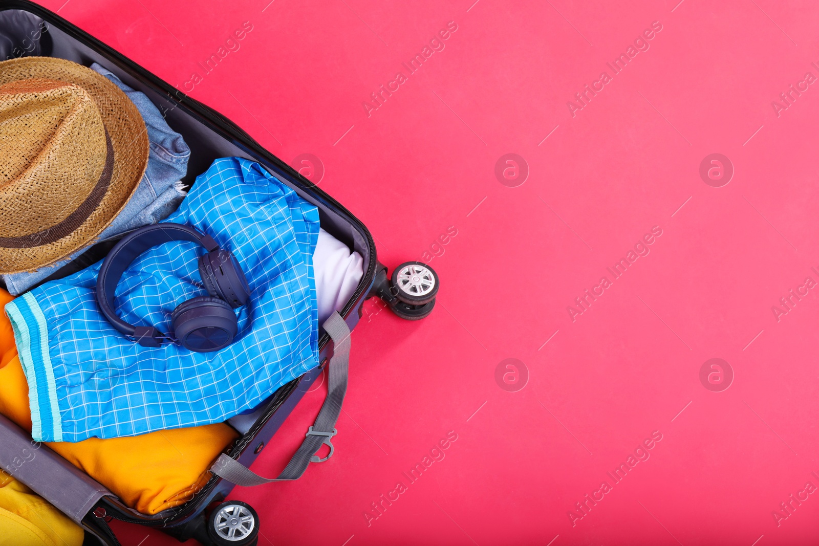 Photo of Travel abroad. Packed suitcase on red background, above view. Space for text