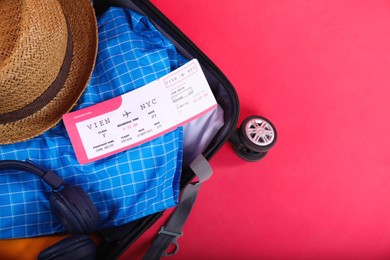 Photo of Travel abroad. Packed suitcase with ticket on red background, above view