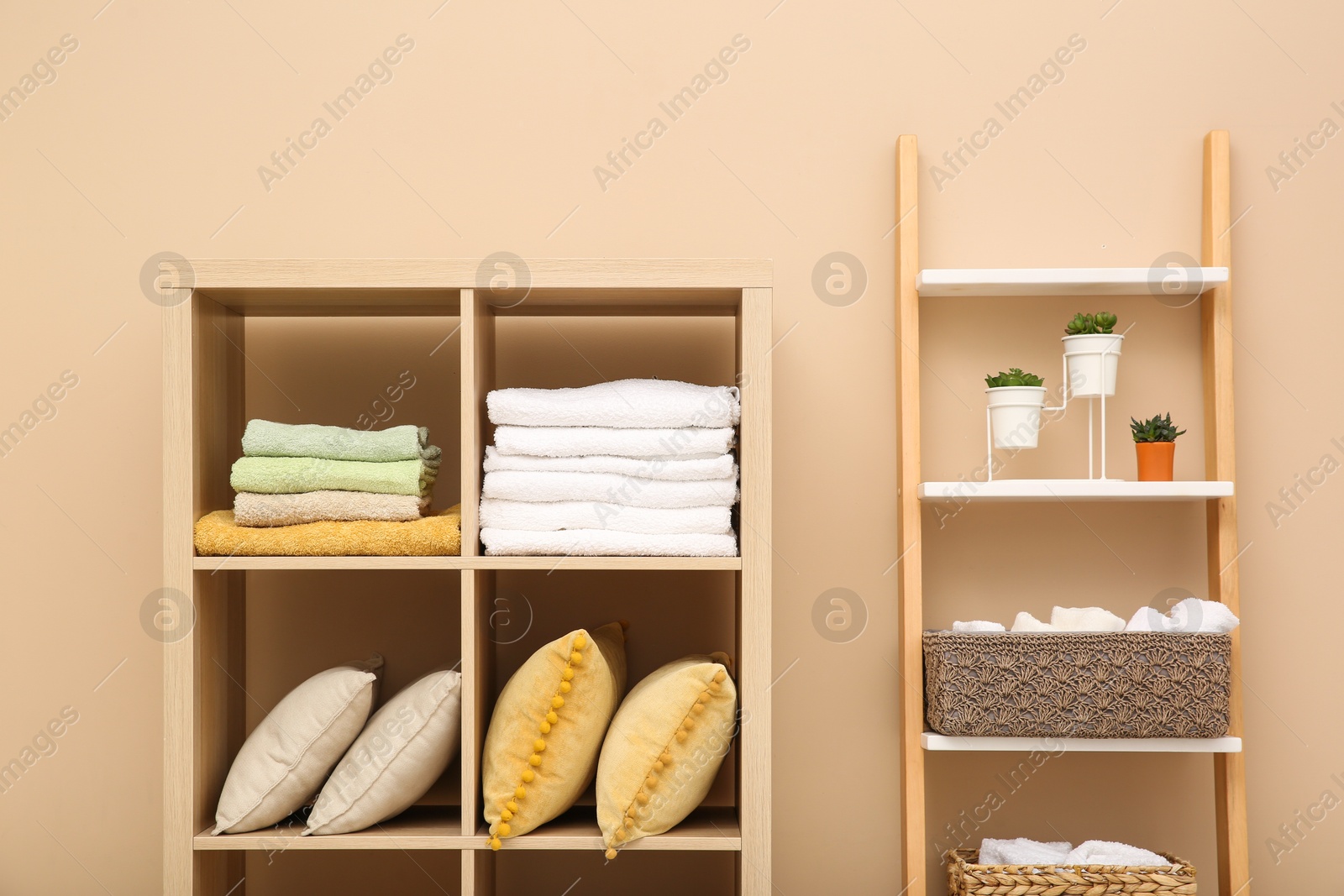 Photo of Folded towels and pillows on shelving unit indoors. Home textile storage