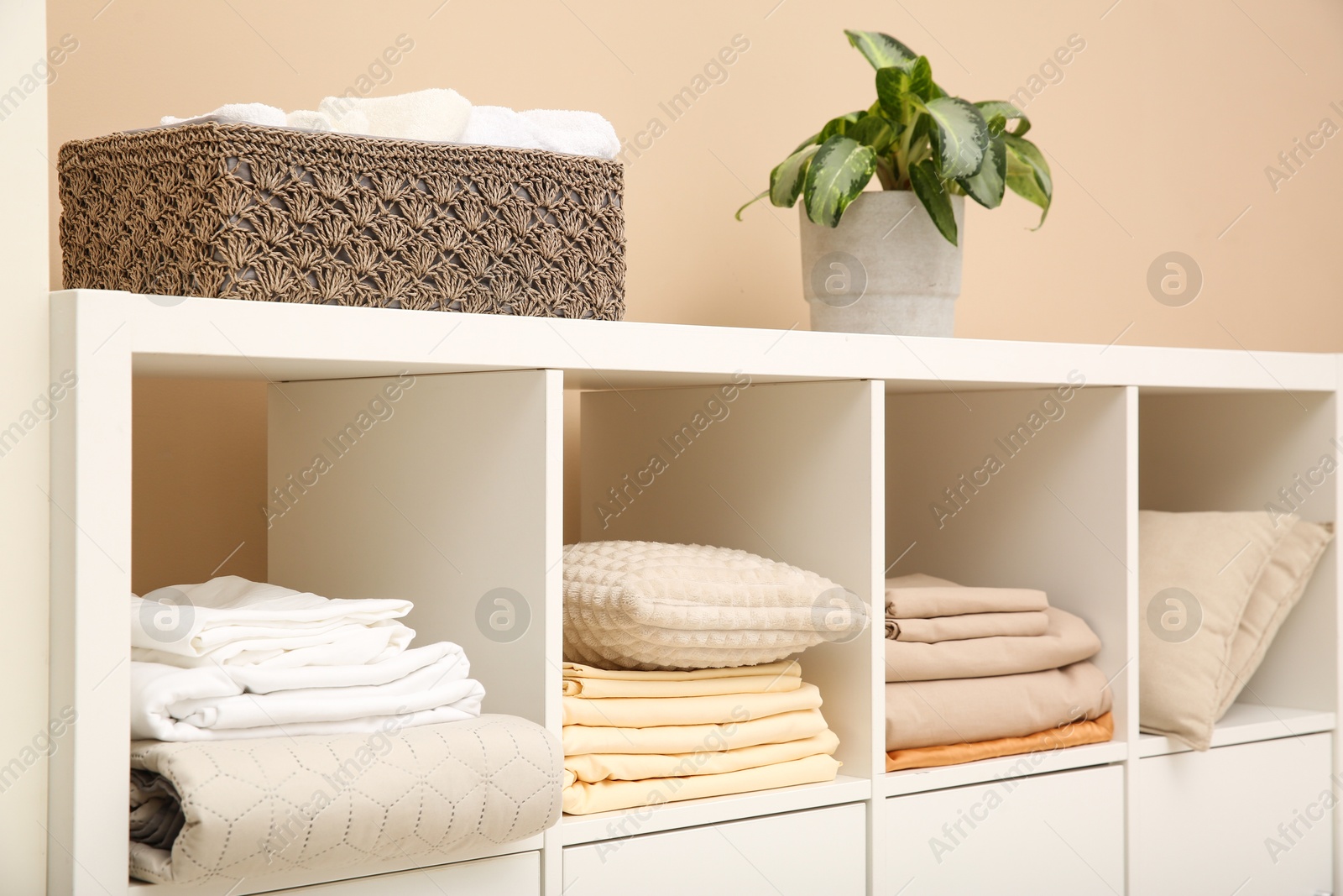 Photo of Folded linens and pillows on shelving unit indoors. Home textile storage