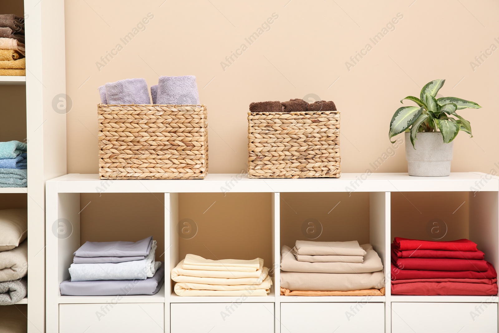 Photo of Folded linens and towels on shelving unit indoors. Home textile storage