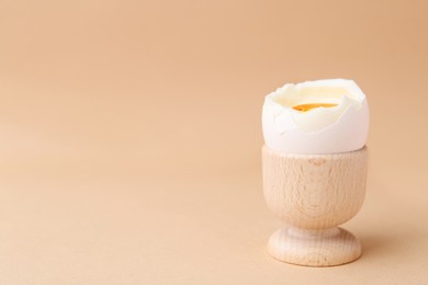 Photo of Soft boiled egg in cup on beige background, space for text