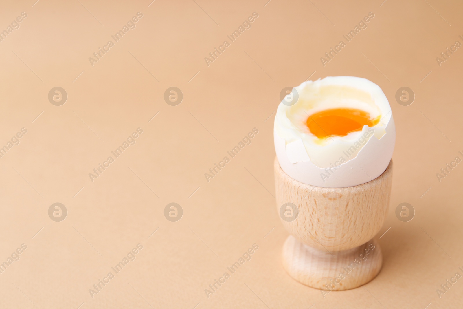 Photo of Soft boiled egg in cup on beige background, space for text