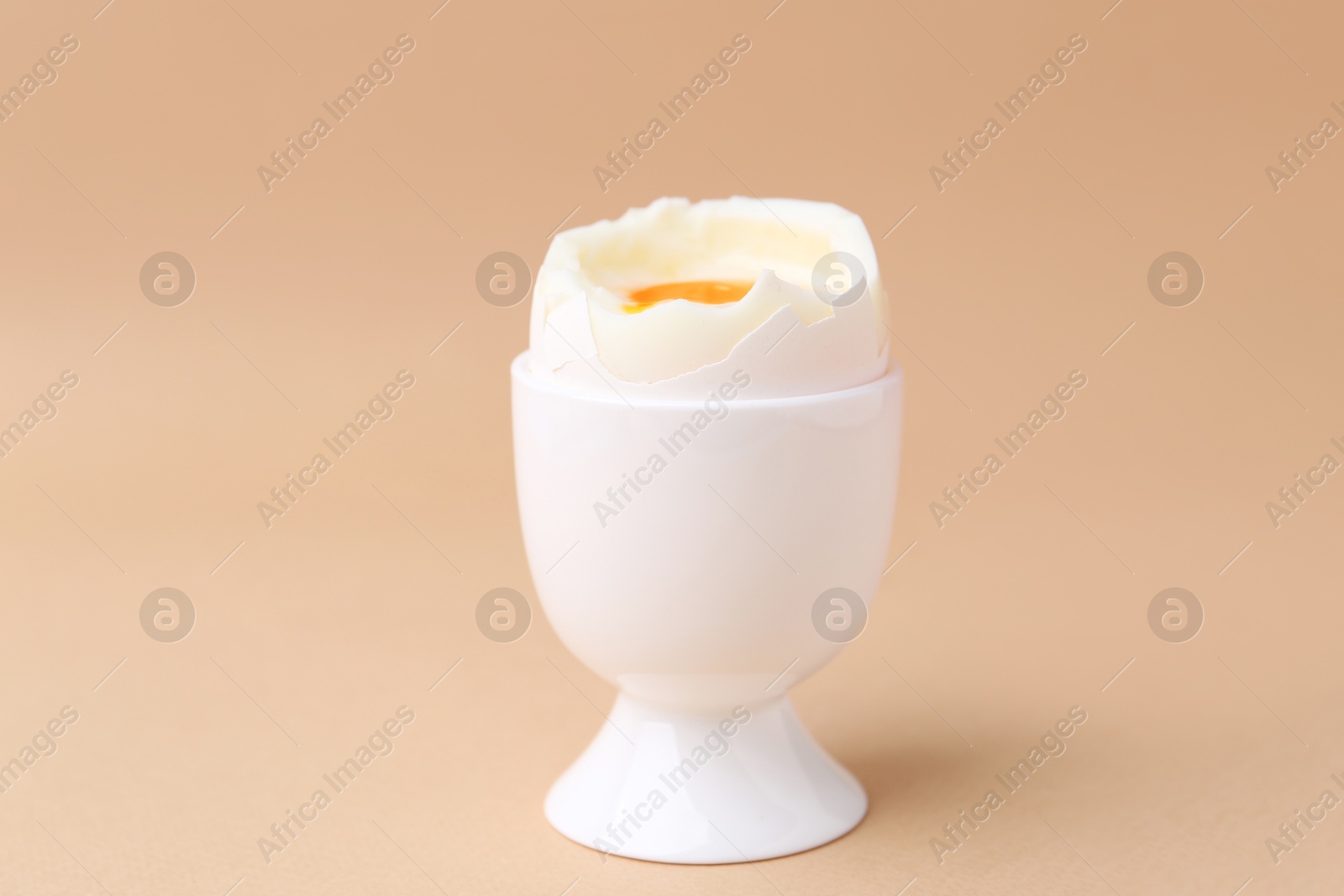 Photo of Soft boiled egg in cup on beige background, closeup