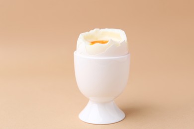 Photo of Soft boiled egg in cup on beige background, closeup