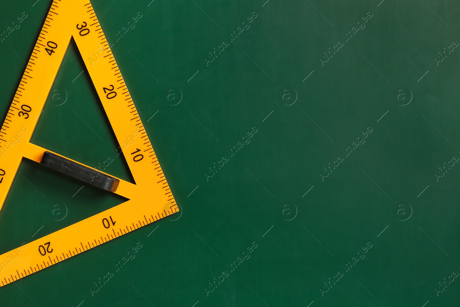 Photo of One triangle ruler on green chalkboard, top view. Space for text