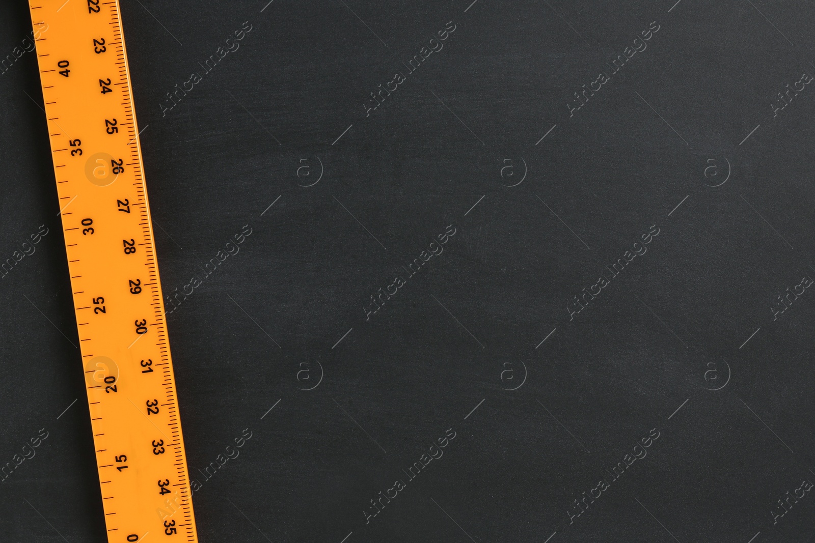 Photo of One ruler on black chalkboard, top view. Space for text