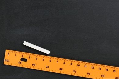 Ruler and chalk on black chalkboard, top view. Space for text