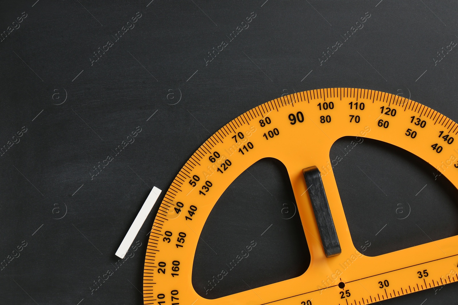 Photo of Protractor ruler and chalk on black chalkboard, top view. Space for text