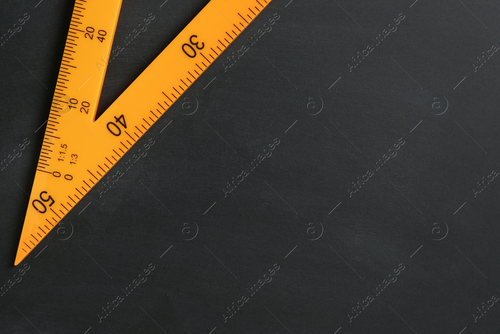 Photo of Triangle ruler on black chalkboard, top view. Space for text