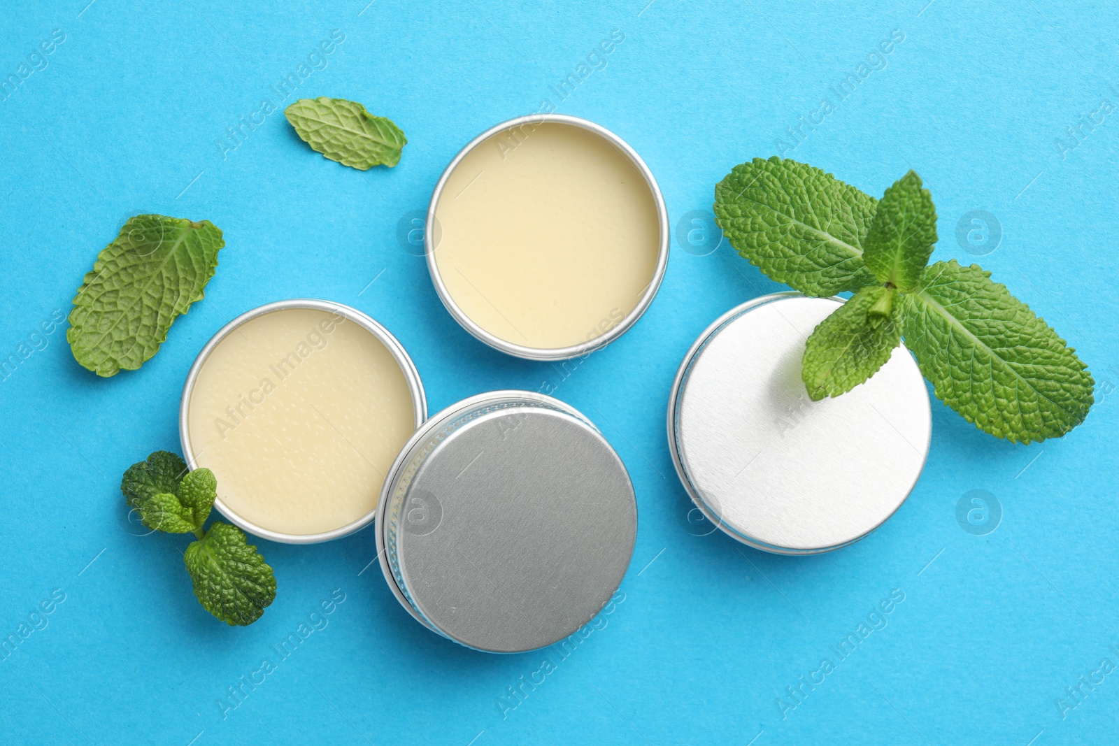 Photo of Natural lip balms and mint leaves on light blue background, flat lay