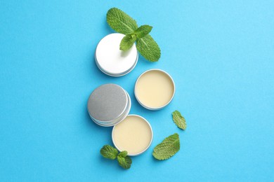 Photo of Natural lip balms and mint leaves on light blue background, flat lay