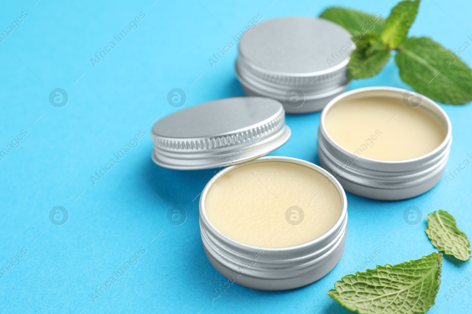 Photo of Natural lip balms and mint leaves on light blue background, closeup