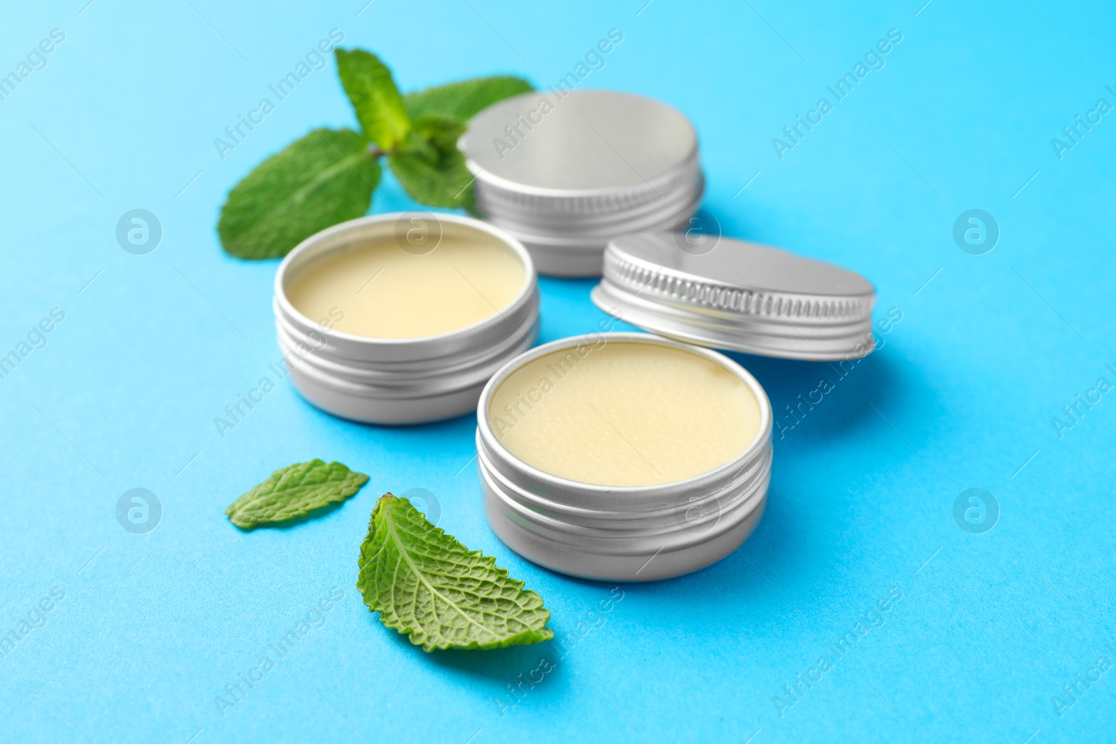 Photo of Natural lip balms and mint leaves on light blue background, closeup