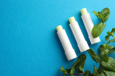 Photo of Natural lip balms and mint leaves on light blue background, flat lay. Space for text