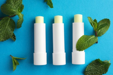 Photo of Natural lip balms and mint leaves on light blue background, flat lay