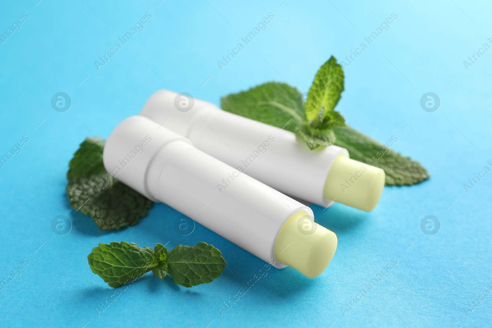 Photo of Natural lip balms and mint leaves on light blue background, closeup