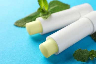 Photo of Natural lip balms and mint leaves on light blue background, closeup