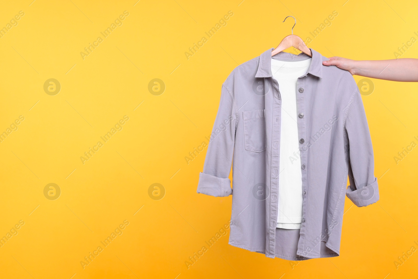 Photo of Woman holding hanger with clothes on yellow background, closeup. Space for text