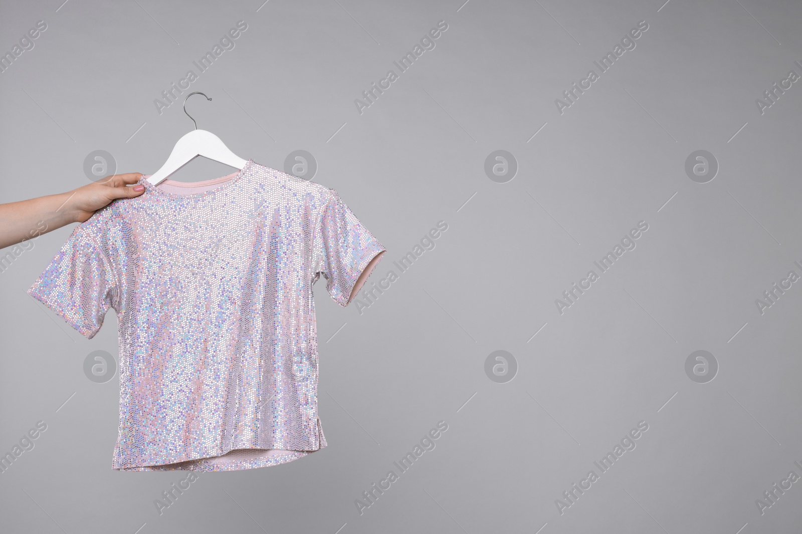 Photo of Woman holding hanger with stylish t-shirt on light grey background, closeup. Space for text