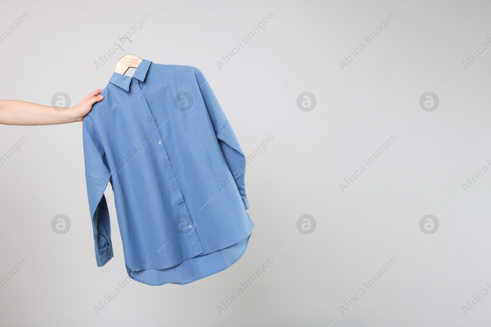 Photo of Woman holding hanger with blue shirt on light grey background, closeup. Space for text