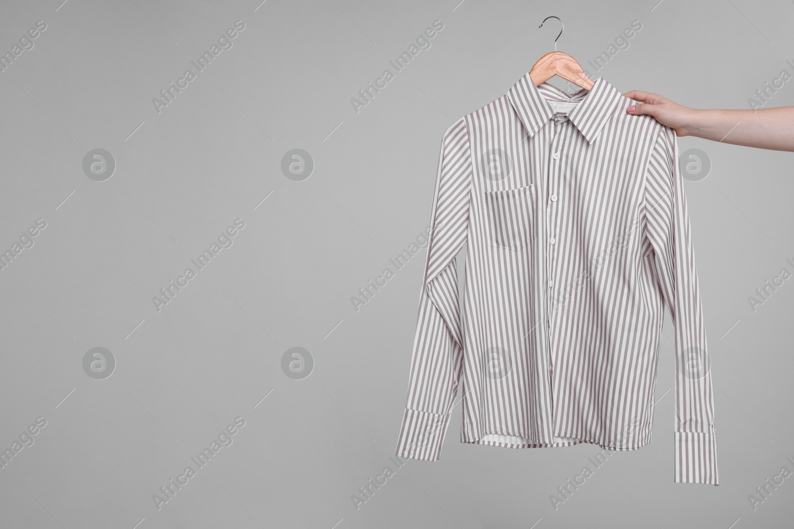 Photo of Woman holding hanger with stylish shirt on light grey background, closeup. Space for text