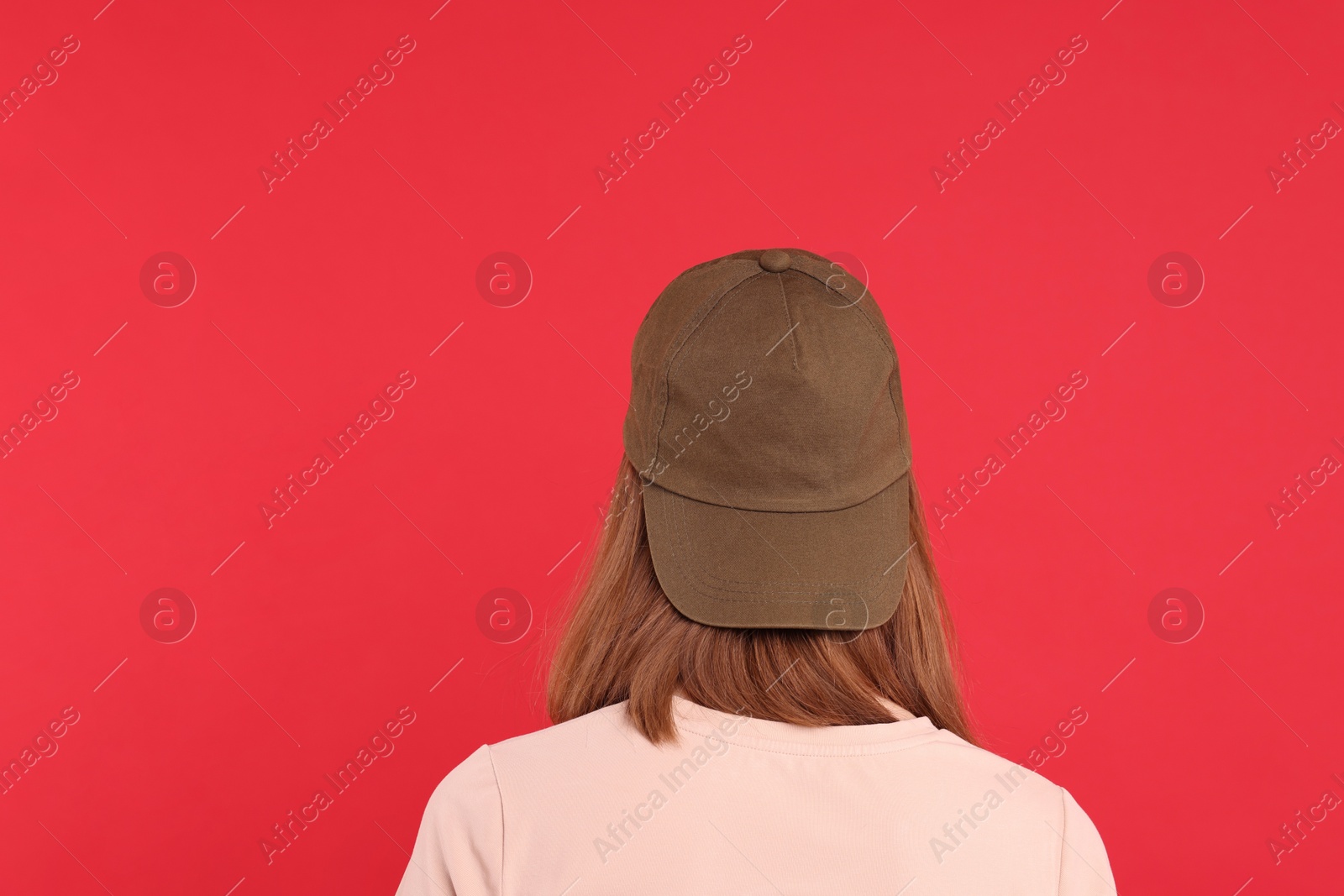 Photo of Woman in stylish baseball cap on red background, back view. Mockup for design