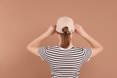 Photo of Woman in stylish baseball cap on beige background, back view. Mockup for design