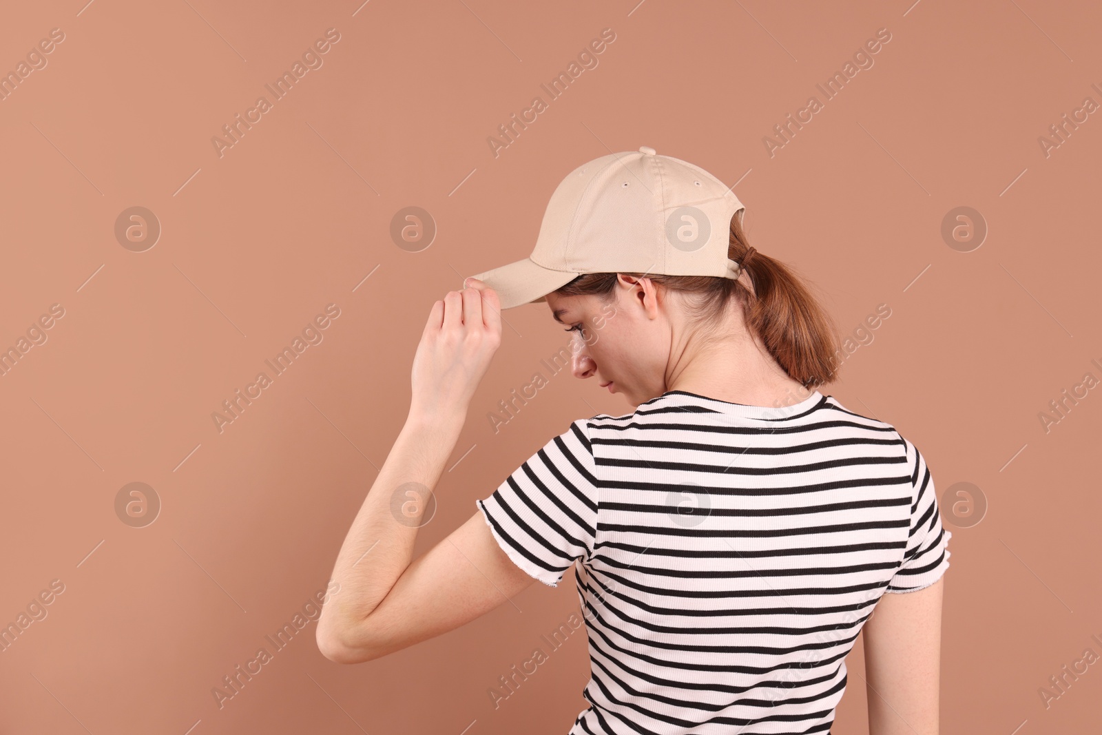 Photo of Woman in stylish baseball cap on beige background, back view. Mockup for design