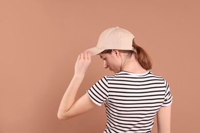 Photo of Woman in stylish baseball cap on beige background, back view. Mockup for design