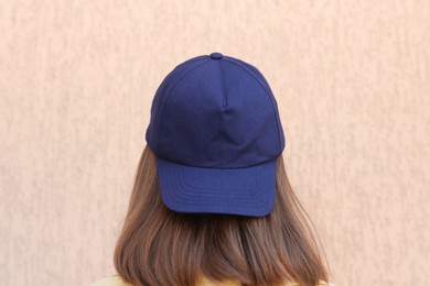 Photo of Woman in stylish baseball cap near beige wall, back view. Mockup for design