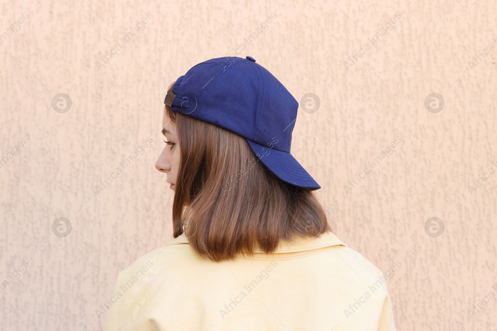 Photo of Woman in stylish baseball cap near beige wall, back view. Mockup for design