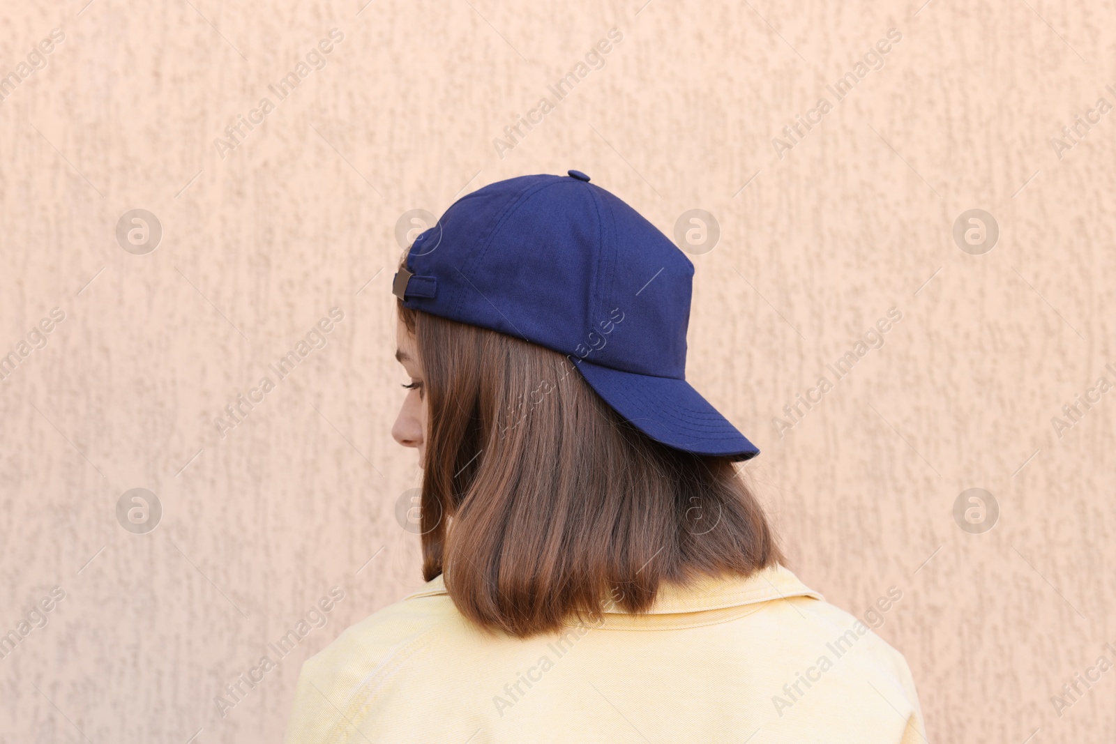 Photo of Woman in stylish baseball cap near beige wall, back view. Mockup for design