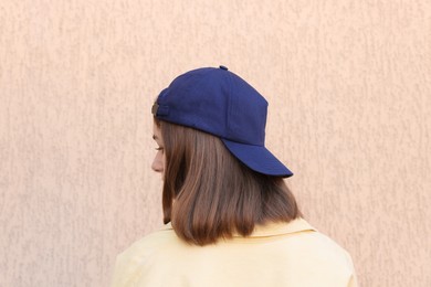 Photo of Woman in stylish baseball cap near beige wall, back view. Mockup for design