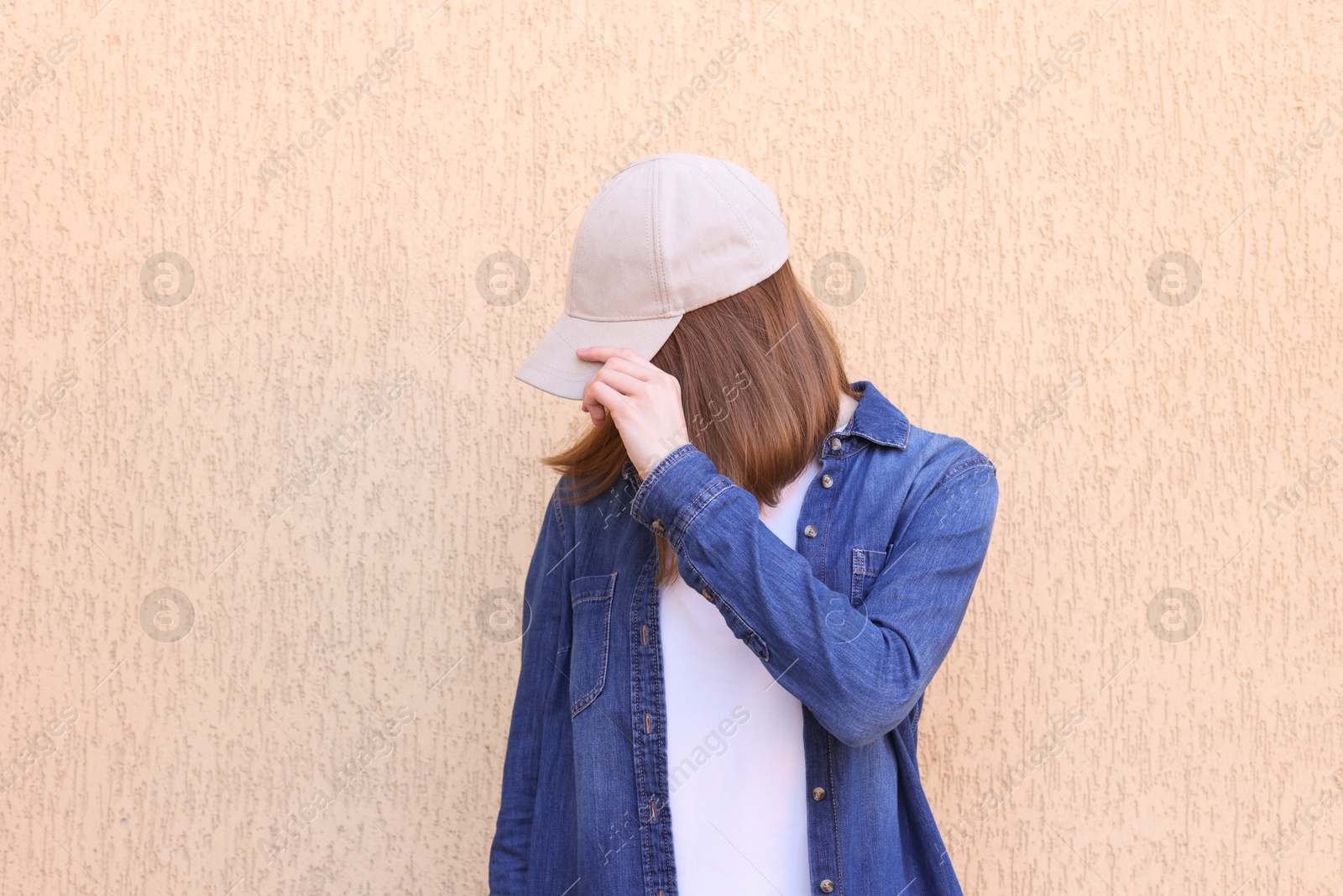 Photo of Woman in stylish baseball cap near beige wall. Mockup for design