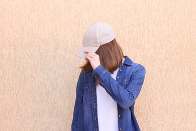 Photo of Woman in stylish baseball cap near beige wall. Mockup for design