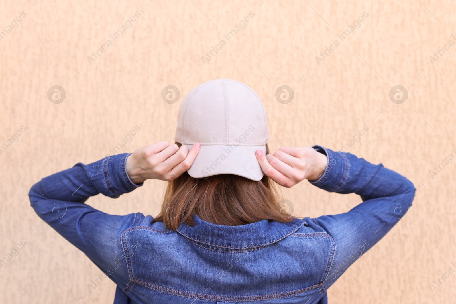 Photo of Woman in stylish baseball cap near beige wall, back view. Mockup for design