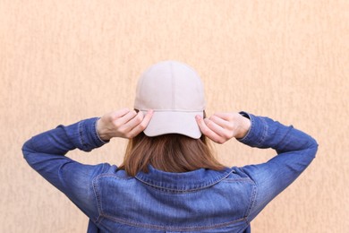 Photo of Woman in stylish baseball cap near beige wall, back view. Mockup for design